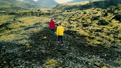 Vista-aérea-de-dos-mujeres-caminando-en-el-campo-de-lava-cubierta-de-musgo-de-Islandia.-Turistas-explorar-el-territorio