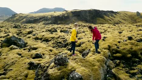 Aerial-view-of-two-woman-standing-on-the-rock,-hiking-together.-Copter-flying-around-tourist-in-lava-field-in-Iceland