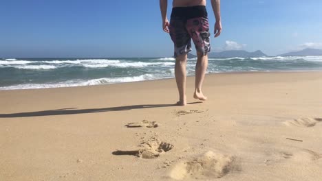 Man-walking-at-the-beach-away-from-camera