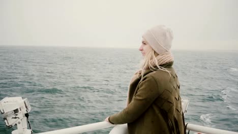 Back-view-of-young-blonde-woman-standing-on-the-ship-and-looking-wistfully-on-the-sea,-exploring-the-Iceland