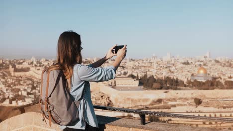 Female-tourist-takes-photos-of-Jerusalem-old-town.-Pretty-Caucasian-traveler-woman-smiling-with-backpack.-Israel.-4K