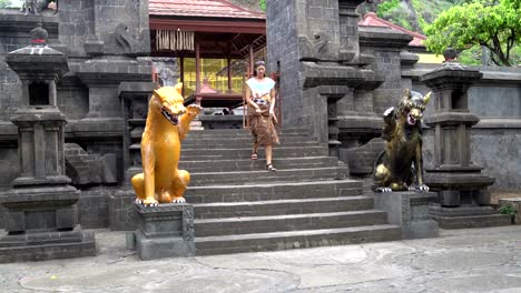 Eine-Frau-in-einem-langen-Rock-ergibt-sich-aus-einem-buddhistischen-Tempel-und-senkt-sich-eine-Steintreppe-mit-Statuen