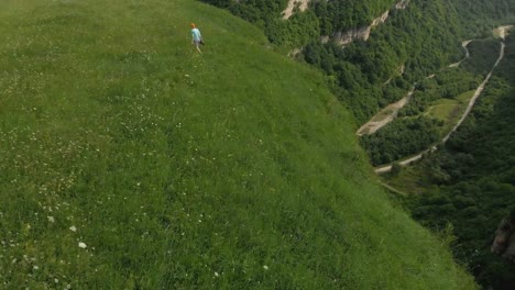 The-girl-photographer-in-glasses-and-a-hat-walks-with-her-dslr-camera-on-the-edge-of-the-plateau-near-the-precipice.-Aerial-view