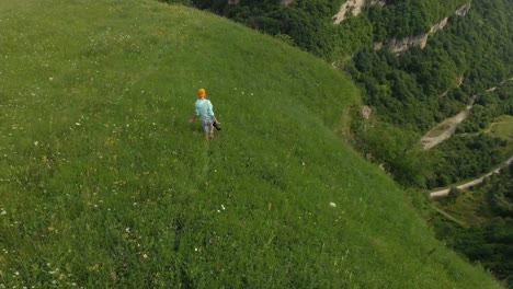 The-girl-photographer-in-glasses-and-a-hat-walks-with-her-dslr-camera-on-the-edge-of-the-plateau-near-the-precipice.-Aerial-view