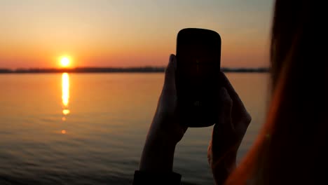 young-woman-is-using-app-in-her-smartphone-for-taking-photo-and-video-of-amazing-sunset