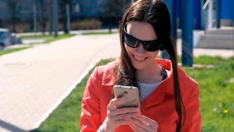 Portrait-of-happy-oung-woman-in-red-coat-waits-for-someone-and-checks-her-phone,-texting.