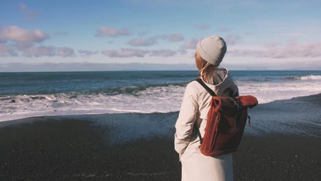 Tourist-woman-with-leather-bagpack-standing-near-the-coastal-landscape-in-Iceland.