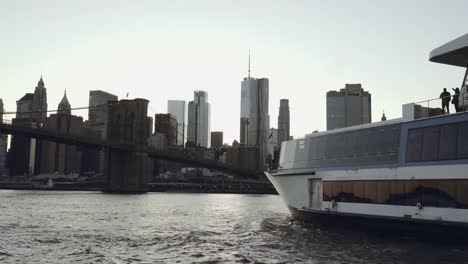 Lower-Manhattan-skyline-with-a-yacht-in-the-foreground-filmed-from-the-boat-in-the-East-River-under-the-Brooklyn-Bridge-in-New-York,-United-States