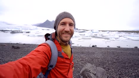 Young-man-taking-selfie-with-glacier-lake,-icebergs-floating-on-water-in-Iceland