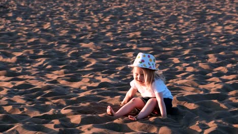 Girl-playing-in-the-sand-sitting-on-the-beach.