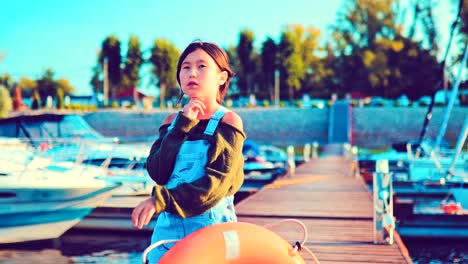 Baby-girl-posing-in-front-of-camera-with-life-buoy-on-quay-of-boats-and-yachts