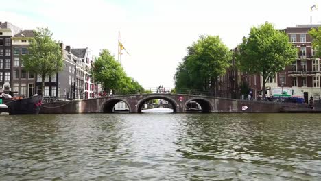 pasando-por-el-emblemático-Puente-tradicional,-vista-del-barco-del-canal-en-Amsterdam,-Holanda-Europa