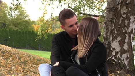 A-young-couple-sits-on-a-white-bedspread-in-autumn-park