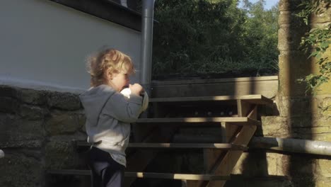 Blond-Toddler-Holding-Ball-Outside-Village-House