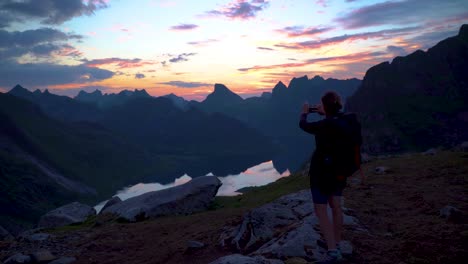 Young-woman-traveler-on-a-background-of-mountains-takes-photos-on-a-mobile-phone