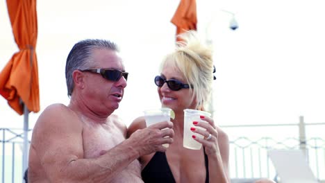 An-older-couple-sitting-by-a-pool-with-drinks