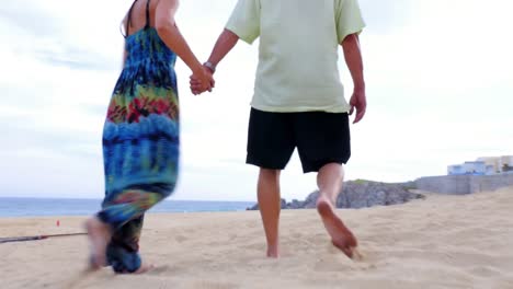 An-older-couple-holding-hands-and-walking-on-the-beach