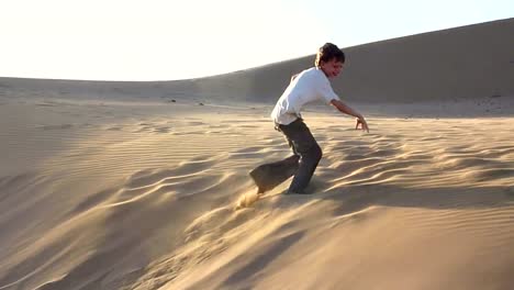 Boy-jumping-and-rolling-down-sanddune,-late-afternoon