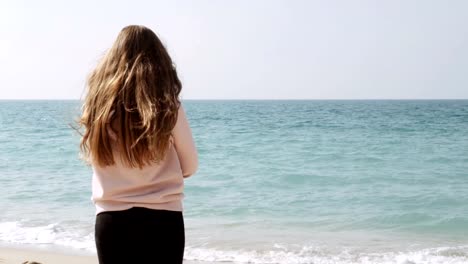 Chica-soñadora-con-largo-pelo-rojo-parado-en-la-playa-y-disfrutando-de-un-increíble-paisaje-marino,-brisa-marina-jugando-con-su-cabello.