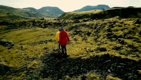 Aerial-view-of-two-female-walking-on-lava-field-covered-moss-in-Iceland,-exploring-the-meadow.-Tourists-hiking-together