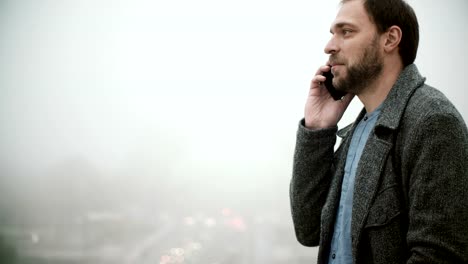 Young-man-standing-near-Eiffel-tower-in-Paris,-France-in-foggy-morning.-Male-talking-on-mobile-phone-with-somebody