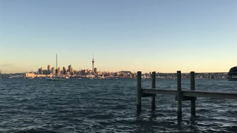 Horizonte-de-la-ciudad-de-Auckland-Nueva-Zelanda-con-un-muelle-de-madera-vacíelo-al-atardecer