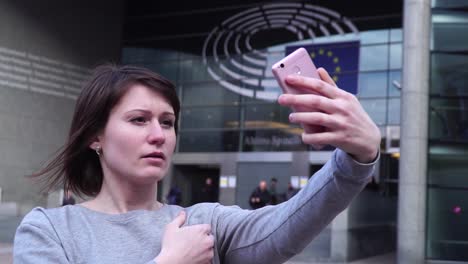 Señora-turismo-hacer-selfie-en-smartphone-cerca-del-Parlamento-Europeo-en-Bruselas.-Bélgica.-cámara-lenta