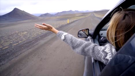 Mujer-caucásica-alegre-dentro-de-auto-en-carretera-de-brazos-extendidos,-paisaje-volcánico-de-la-montaña.-Concepto-de-viaje-de-carretera.--Chica-cabello-rubio-en-el-paisaje.-CÁMARA-LENTA