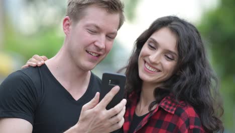 Young-couple-using-phone-together-outdoors