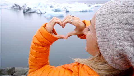 Junge-Frau-macht-Herz-Form-Finger-Frame-auf-Gletscherlagune-Islands-zeigen,-Liebe-und-Mitgefühl,-Natur