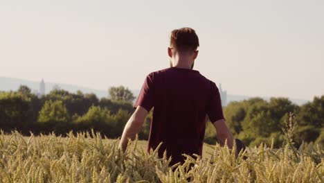 Adult-walking-through-Beautiful-wheat-field-holding-skateboard-with-city-in-background---shot-on-RED