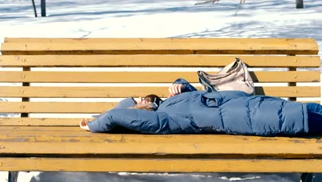 Joven-cansada-se-duerme-en-el-parque-en-un-banco-en-el-invierno.