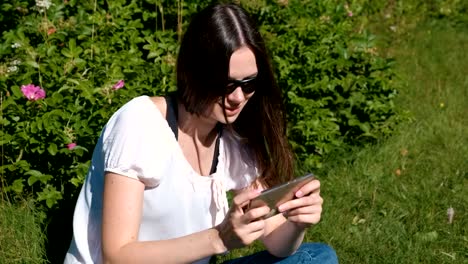 Woman-is-playing-a-game-on-mobile-phone-sitting-in-park-in-sunny-day.