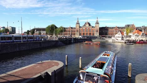 Icónica-escena-holandesa,-barco-turístico-en-el-centro-de-la-canal-por-la-estación-Central-de-Ámsterdam,-de-Europa.