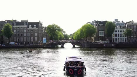 Canal-cruise-tour-barco-velas-en-canal-de-los-emblemático-con-el-tradicional-puente-en-Amsterdam,-Holanda-Europa