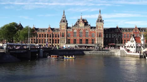 Traditional-boats-at-canal-waterfront-in-front-of-Amsterdam-Central-station,-Europe.