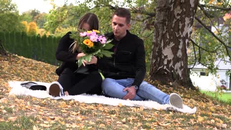 A-young-couple-sits-on-a-white-bedspread-in-autumn-park