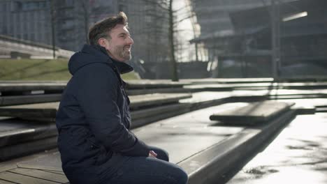 Middle-aged-man-is-siiting-on-a-bench-in-modern-urban-city-in-autumn