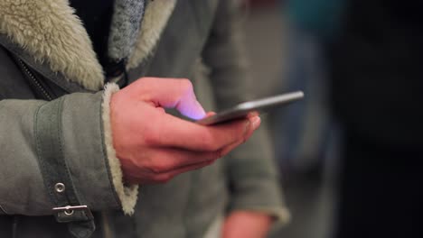 Commuter-person-holding-cellphone-device-browsing-the-internet-on-smartphone-checking-emails-texting-friends-while-on-underground-subway-platform-in-4K