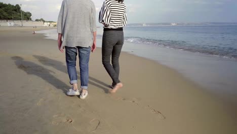 Mature-women-walking-on-wet-sand-on-seashore.