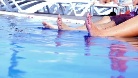 A-man's-and-a-woman's-feet-splashing-at-the-edge-of-a-pool