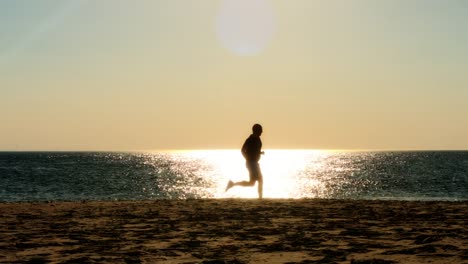 corredor-masculino-corriendo-en-la-playa,-silueta-de-la-puesta-de-sol,-cámara-lenta