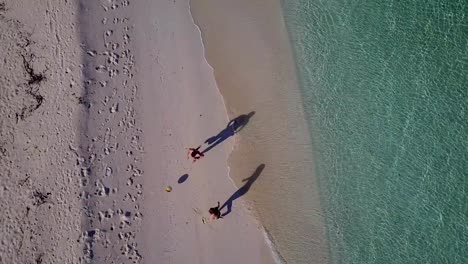 v03814-Aerial-flying-drone-view-of-Maldives-white-sandy-beach-on-sunny-tropical-paradise-island-with-aqua-blue-sky-sea-water-ocean-4k-2-people-young-couple-man-woman-playing-ball-fun-together