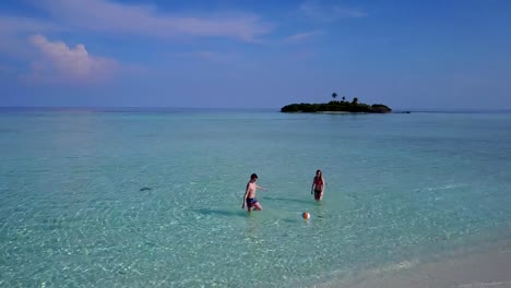 v03817-vista-aérea-de-drone-volador-de-playa-en-isla-paraíso-soleado-con-cielo-azul-aqua-mar-agua-océano-4k-2-personas-pareja-hombre-mujer-tocando-juntos-diversión-bola-blanco-Maldivas