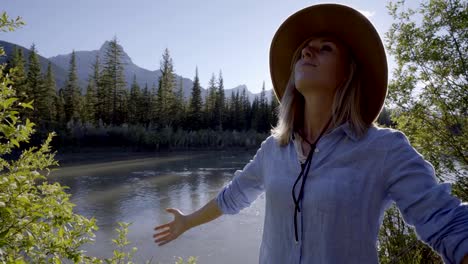 Young-woman-practicing-breathing-exercise-by-the-river-surrounded-by-nature