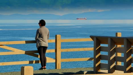 Woman-Viewing-Boat-on-Wide-Ocean-Sea,-Olympic-Mountains-Background