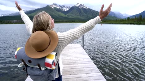 Mujer-joven-está-parado-en-el-embarcadero-de-madera-sobre-hermosa-montaña-lago-brazos-extendidos-para-la-libertad.