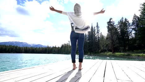 Young-woman-arms-outstretched-on-lake-pier,-Canada