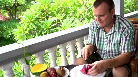 Mann-auf-dem-Balkon-sitzen-reinigt-die-Pitahaya-Frucht-und-isst