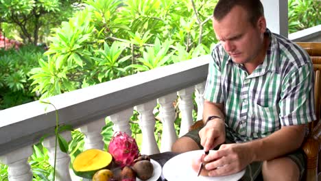 Man-sitting-on-the-balcony-cleans-the-passion-fruit-and-eats